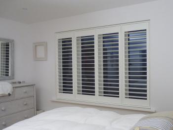 Four Panel White Window Shutters In Bedroom