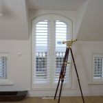 Telescope Looking Out Arched Window With White Plantation Shutters