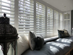 White Louvered Shutters In Large Square Bay Window With Cushioned Seat